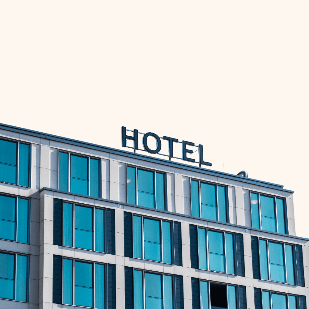 Modern hotel building with "Hotel" sign on the roof. Blue-tinted glass windows cover the facade, reflecting a minimalist and contemporary design.