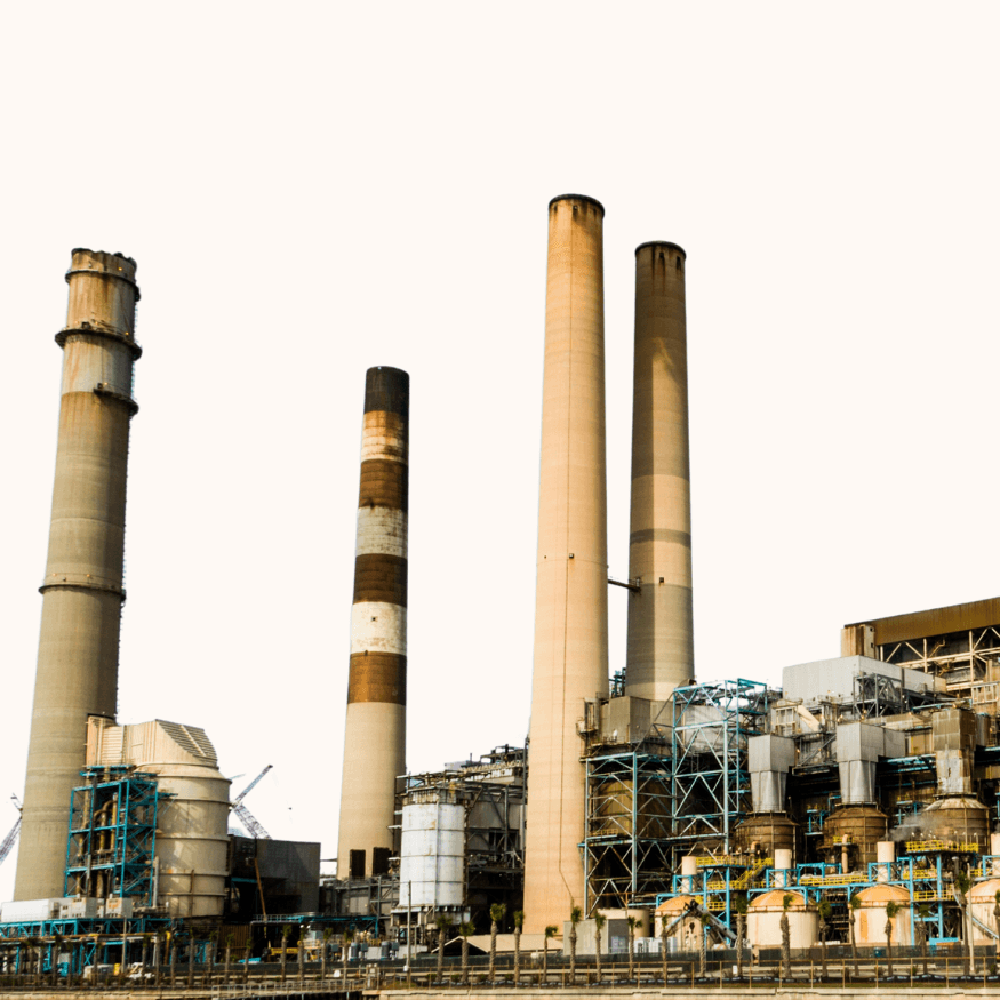 Tall industrial smokestacks rise from a sprawling factory complex. The sky is clear, contrasting with the gritty, industrial landscape below.