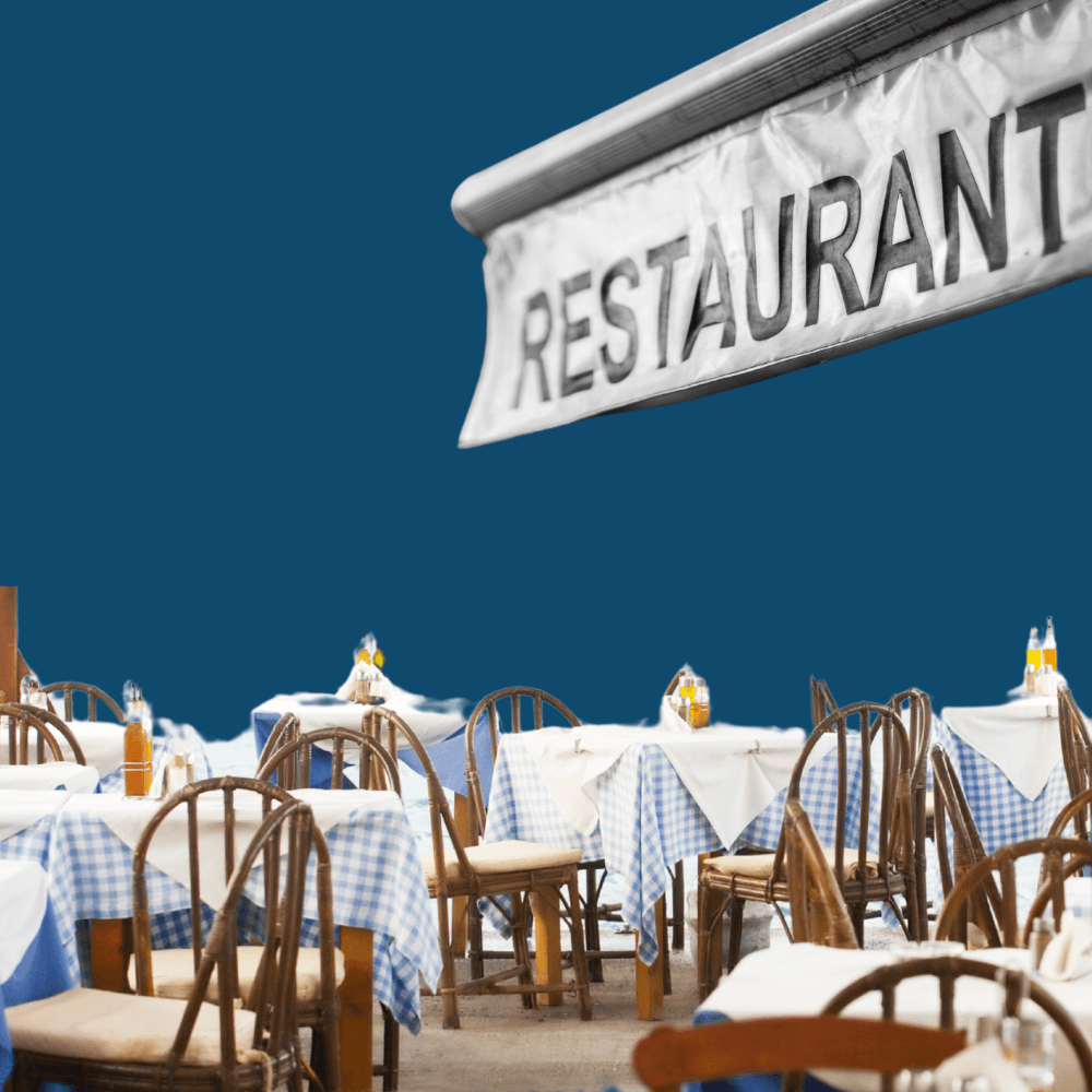 Outdoor dining area with empty wooden chairs and tables covered in blue and white checkered cloths. A "RESTAURANT" sign hangs above, evoking a cozy, inviting atmosphere.