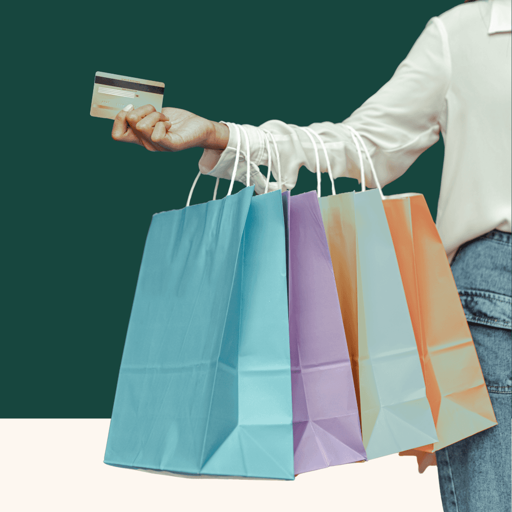 A person in a white shirt holds colorful shopping bags and a credit card against a dark green background, conveying a joyful shopping experience.